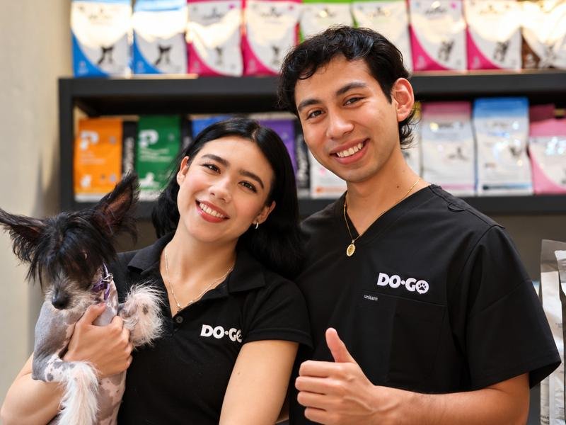 Dos colaboradores de DOGO Pet Store con uniforme, sonriendo junto a un perro en la tienda