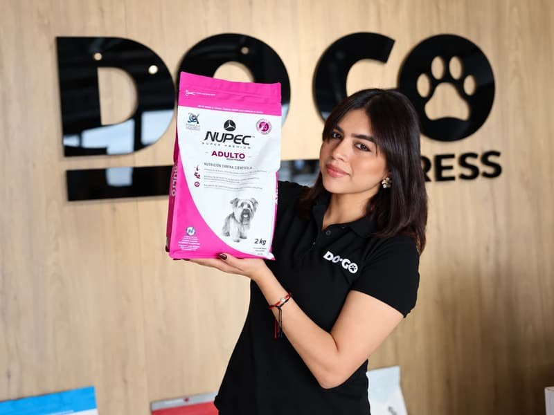 Colaboradora de DOGO Express mostrando un alimento Nupec Adulto razas pequeñas de 2 kg frente al logo de la tienda