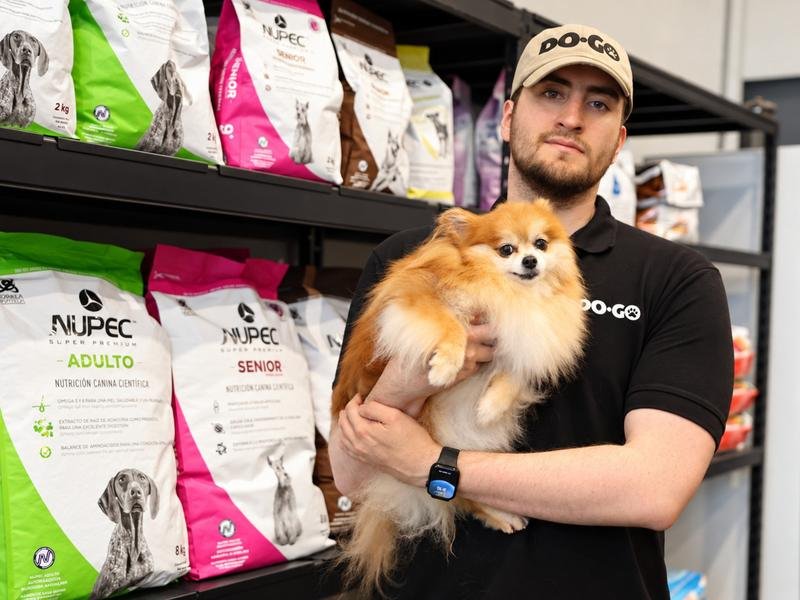 Colaborador de DOGO cargando un pomerania frente al anaquel de alimento Nupec